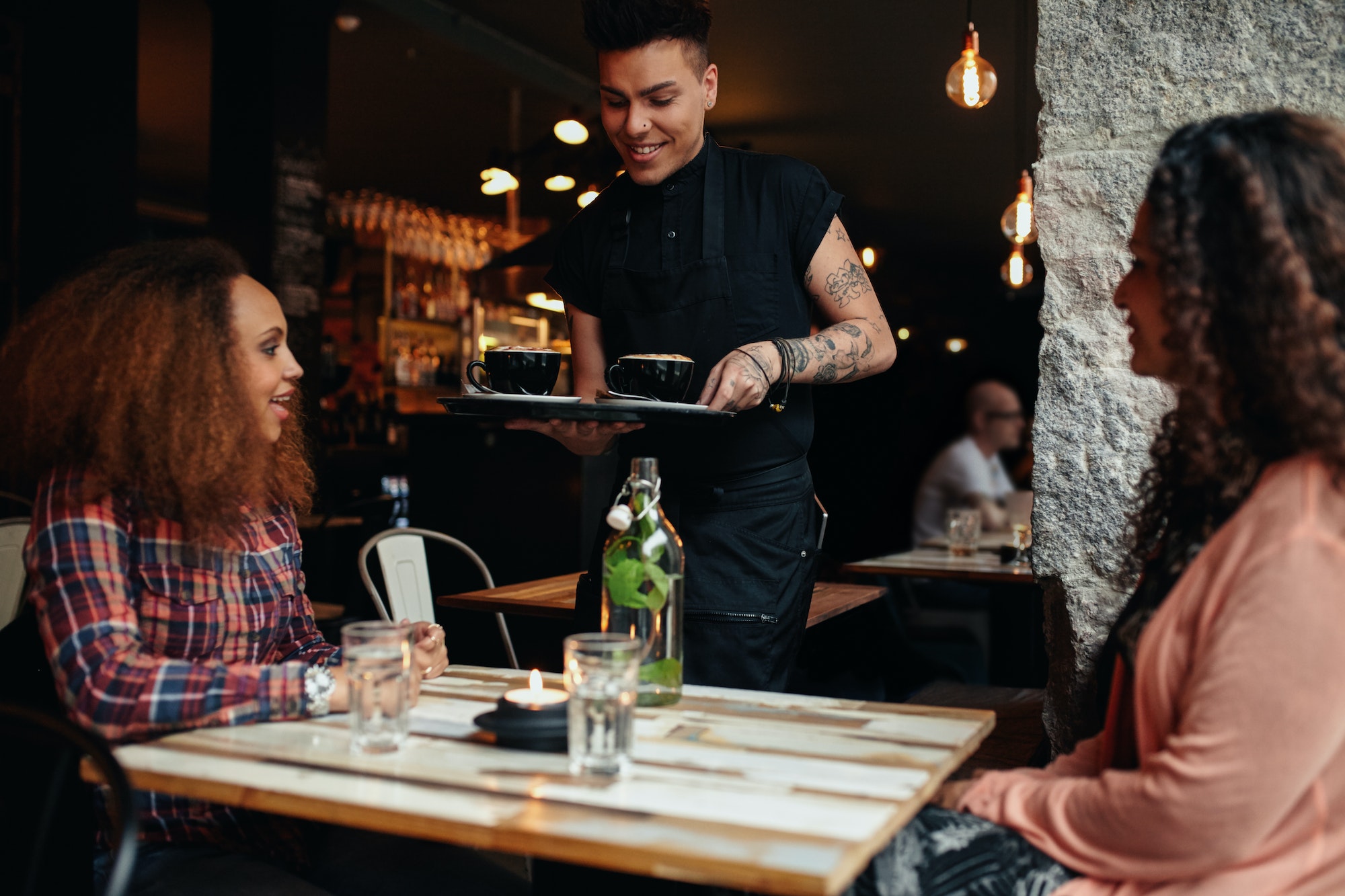 Waiter serving coffee to customers at cafe