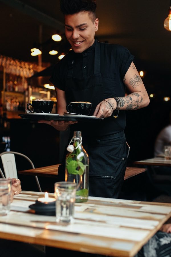 Waiter serving coffee to customers at cafe